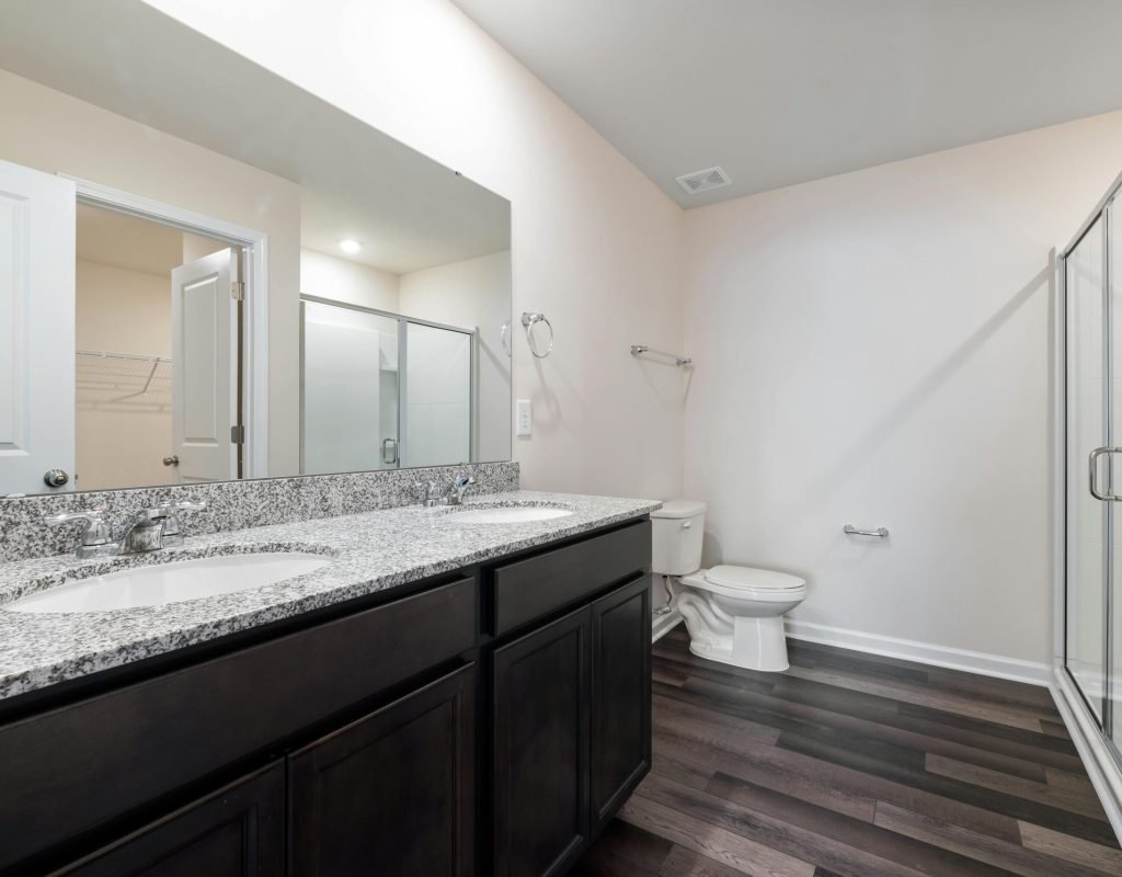 Elegant modern bathroom featuring granite countertops, glass shower, and hardwood floor for a sleek interior.