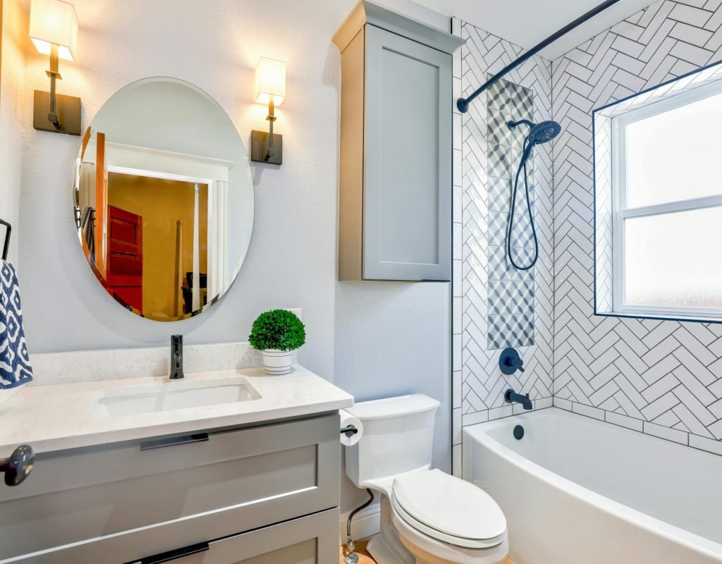 Elegant modern bathroom featuring chevron tiles, oval mirror, and sleek fixtures for a contemporary look.